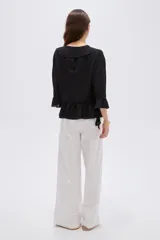 Blusa de poliéster color negro, con diseño holgado, escote en V con solapa y volados que descienden en cascada por el frente. Cuenta con mangas 3/4 con detalles de volados en los puños y en el ruedo.