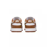 Championes Nike Dunk Low con diseño bicolor en blanco y marrón. Presentan una silueta clásica de perfil bajo, confeccionados en cuero con el icónico logo de la marca en los laterales, cierre de cordones y suela de goma resistente.