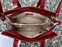 Cartera mini tote de cuero vacuno color bordó, con acabado charol, doble asa de mano y estructura rígida.