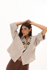 Camisa de textura plisada en color beige, con cuello clásico, cierre frontal de botones y mangas tres cuartos con puños vueltos.