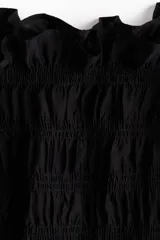 Blusa negra de tejido fruncido con escote bote, mangas cortas abullonadas con terminación elástica y bajo con ligero vuelo.