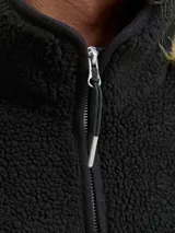 Campera tipo teddy de cuello alto y manga larga, confeccionada en tejido de textura suave. Presenta cierre frontal completo, bolsillos laterales con cierre y un pequeño bordado en el pecho.