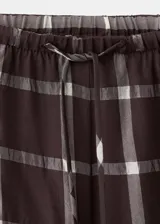 Pantalón balloon de tiro medio en color marrón oscuro con estampa de cuadros. Cuenta con cintura ajustable con goma y cierre de lazo, además de dos bolsillos laterales y diseño abuchonado en los tobillos.