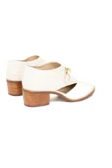 Zapato de cuero color blanco hueso con diseño de texturas combinadas, presentando un acabado tipo reptil en la parte trasera y cuero liso en la puntera. Cuenta con un corte lateral, cierre mediante hebilla dorada y tacón cuadrado de madera.