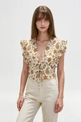 Blusa de diseño estampado con motivos florales y cachemira en tonos marrones sobre base blanca, con escote en V profundo y doble lazo frontal ajustable. Presenta mangas cortas con volados.