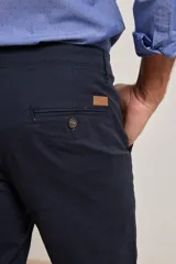 Pantalón de vestir verde oliva, de corte slim fit, sin pinzas, con bolsillos laterales y traseros. Se ajusta a la cintura con cinturón de cuero marrón.