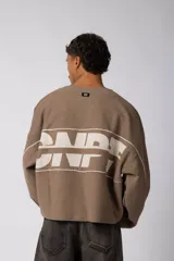 Buzo oversize de corte boxy, confeccionado en algodón rústico de alto gramaje en color beige. Presenta cuello redondo con borde crudo, mangas largas y una estampa frontal con el texto VCP delimitado por líneas horizontales blancas.