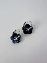 Aros de acero quirúrgico con argolla mediana y dije colgante en forma de flor de resina marmolada en tonos negros y grises.