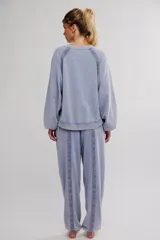 Conjunto de pijama de frisa lavada color celeste, compuesto por un buzo de calce amplio con escote redondo, mangas raglán abullonadas y puntilla aplicada sobre las costuras, y un pantalón de cintura elastizada con cordón, puños en los tobillos y detalles de puntilla en los paneles.