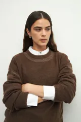 Sweater de tejido de punto color marrón, con cuello redondo y detalles de calados decorativos en el cuello y las mangas. Presenta un diseño de corte recto y manga larga.