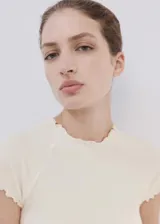 Camiseta cruda de manga larga con cuello redondo y diseño ajustado, con terminaciones onduladas en contraste marrón en cuello y dobladillo.