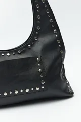 Cartera tipo hobo de símil cuero texturizado color marrón oscuro, con apliques de tachas metálicas plateadas que recorren el frente y el contorno. Cuenta con un bolsillo frontal y un asa de hombro.