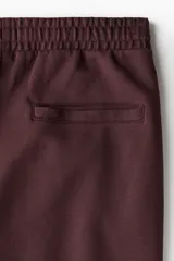 Jogger color bordó en tejido suave de mezcla de algodón, con pliegue cosido en la parte delantera. Presenta cintura elástica con cordón ajustable, bolsillos laterales y un bolsillo insertado en la parte trasera.