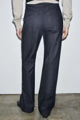 Jeans de tiro medio con corte flare y largo completo. Presenta bolsillos delanteros, cierre con cremallera, botón y ganchos metálicos.