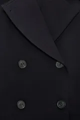 Trench corta de color negro con cuello de solapa, cierre frontal cruzado con botones y mangas largas con trabillas ajustables. Cuenta con bolsillos delanteros de vivo.