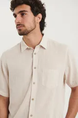 Camisa sport de manga corta, confeccionada en una mezcla de lino y algodón. Presenta cuello clásico, cierre frontal con botones de coco y un bolsillo aplicado en el pecho.