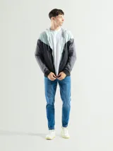 Campera deportiva negra de nylon impermeable con capucha y cierre frontal. Presenta puños y cintura elásticos de tejido acanalado. Tiene un pequeño logo blanco en el pecho.