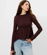Blusa de encaje color bordó con trama floral y transparencia. Presenta cuello medio, mangas largas ajustadas y un recorte debajo del busto que genera un efecto peplum con volados en el dobladillo.