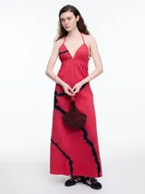 Vestido largo de algodón color rojo con estampado tie-dye en negro. Tiene escote halter con tirantes finos ajustables en la espalda y escote en V profundo tanto en la parte delantera como en la trasera.