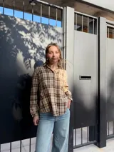 Camisa de corte holgado con estampado de cuadros escoceses en tonos beige y marrón. Presenta cuello clásico, cierre frontal con botones y mangas largas.