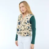 Chaleco sin mangas confeccionado en tejido tipo corderito, con estampado floral en tonos azules y verdes sobre base beige. Presenta escote en V, cierre frontal con botones a presión y ribetes en color crema.