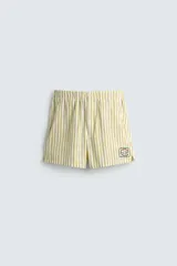 Shorts de hombre confeccionados en algodón con estampado de rayas verticales amarillas y blancas. Presenta cintura elástica, bolsillos frontales y un pequeño bordado de un pez en la parte inferior derecha.