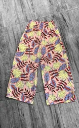 Pantalón tipo palazzo de corte amplio y tiro alto con cintura elástica. Presenta un estampado colorido de hojas sobre fondo rosado.