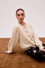 Cárdigan color crudo con botones dorados, cuello redondo y bolsillos frontales.