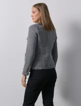 Chaqueta Nanette de tejido tweed color beige, con cuello a la base, abertura central y bolsillos delanteros. Tiene apliques de botones perlados en los puños, terminación desflecada y forro interno.