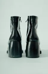 Bota corta de cuero negro, con caña media y punta cuadrada. Se caracteriza por su taco geométrico y voluminoso, con acabado texturado.