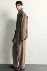 Pantalón relaxed fit de hombre color marrón con textura estructurada, cintura con pliegues frontales, bolsillos laterales y cierre frontal con cremallera y botón.