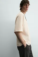 Camiseta de manga corta color crema, con cuello redondo y tejido acanalado verticalmente, de corte holgado (boxy fit).