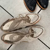 Zapato tipo sueco de cuero vacuno negro con textura reptil, con cordones y talón descubierto. Tiene suela de madera con altura de 4,5 cm en el talón y 1,5 cm en la parte delantera.