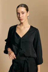Blusa negra de satén con escote en V y detalle de volados frontales. Presenta mangas largas con puños abotonados y una silueta fluida.