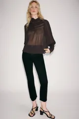 Blusa de cuello subido y manga larga, color marrón oscuro, con detalles de bordados combinados a tono en el canesú y los puños anchos. Cierre en la espalda con abertura y botones.