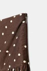 Pantalón de tiro alto con pernera ancha y diseño fluido. Presenta un estampado de lunares blancos sobre fondo marrón y detalle de frunces en la cintura.