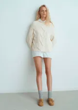 Sweater de punto grueso color crema con diseño de trenzas verticales, cuello perkins y corte oversize.