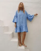 Vestido corto de lino color celeste, con cuello mao, cierre frontal abotonado con botones de nácar, mangas tres cuartos acampanadas con volados y falda con volante en el dobladillo.