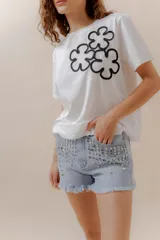 Short de jean celeste con tachas metálicas plateadas, tiro medio, terminaciones desflecadas, cierre frontal y bolsillos funcionales.