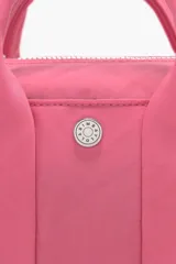 Bolso bandolera de nylon color rosa, con forma cilíndrica, tamaño mini, cierre de cremallera y asa tejida regulable. Exterior personalizado con logo metálico.