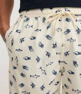 Bermuda de baño para hombre, color crema, con estampado repetitivo de peces azules. Presenta cintura elástica con cordón de ajuste y forro interior de malla.