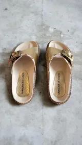 Sandalias de cuero dorado marca Carolina De Cunto, con tira ancha ajustable mediante hebilla metálica grande personalizada y detalles pintados a mano. Suela de goma eva ligera.