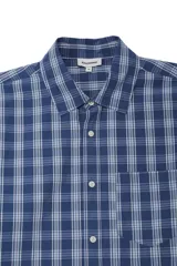 Camisa de mangas largas color azul con estampado a cuadros blancos, de corte boxy. Presenta cierre frontal con botones, cuello con solapa y un bolsillo en el pecho.