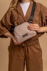 Bandolera pequeña de diseño minimalista confeccionada en tafeta liviana color beige. Cuenta con cierre superior, correa ancha ajustable de color negro y etiqueta frontal con el logo de la marca Lincoln's.