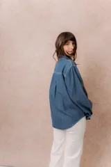Camisa de denim liviano con calce relajado, cuello camisero clásico y cierre frontal con botones. Presenta una destacada aplicación de strass en el frente formando un diseño de alas.