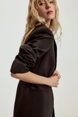 Blazer entallada de cuello solapa y manga larga con hombreras. Presenta bolsillos delanteros de vivo y cierre frontal con un botón metálico decorativo.