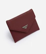 Billetera tipo sobre Satinato color bordó, de formato compacto y estructura plegable. Con textura en relieve, solapa frontal y aplique metálico triangular con el nombre de la marca grabado.