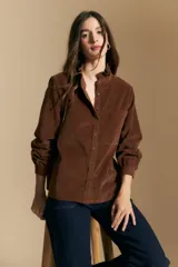 Camisa de pana color crema con cuello camisero con volados, cierre frontal de botones y mangas largas con puños abotonados. Presenta un bolsillo aplicado en el pecho y una silueta relajada.