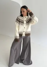 Cardigan de tejido de punto con diseño jacquard de inspiración nórdica. Presenta un patrón geométrico en tonos crema y marrón, cuello redondo y cierre frontal con botones.