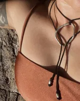 Collar con dije colgante de forma orgánica e irregular, acabado dorado, suspendido de un cordón negro de algodón natural.